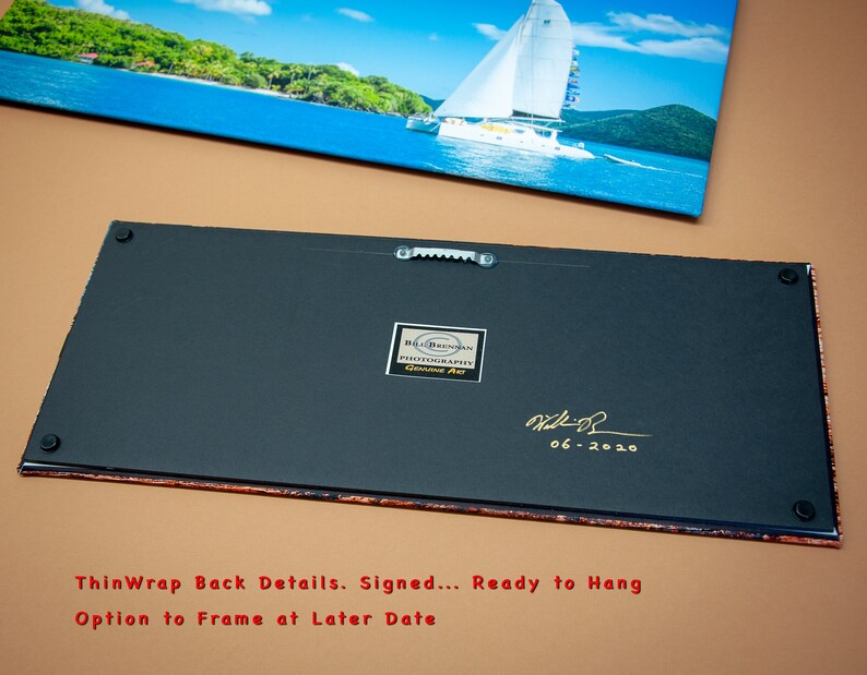 May include: A rectangular canvas print depicting a tropical ocean scene with a sailboat. The back of the canvas is visible, showing a black surface with a sawtooth hanger, a label, and a signature dated 06-2020. The text reads "ThinWrap Back Details. Signed... Ready to Hang Option to Frame at Later Date."