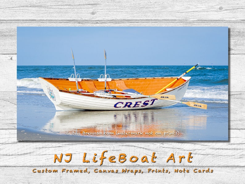 May include: A white and orange lifeboat, labeled "CREST", rests on a sandy beach with the ocean in the background. Two oars and two tall poles are visible. The image is a print of NJ LifeBoat Art.
