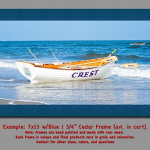 K&ouml;nnte beinhalten: Ein gerahmter Druck mit einem wei&szlig;en Boot mit dem Wort "CREST" an der Seite, das an einem Sandstrand liegt. Das Boot hat eine orangefarbene Innenausstattung und befindet sich in der N&auml;he von Meereswellen. Der Rahmen ist dunkelblau.
