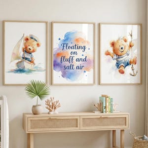 Puede incluir: Conjunto de tres láminas enmarcadas en acuarela con temática náutica. Una lámina muestra un oso de peluche navegando en un barco, otra tiene el texto "Floating on fluff and salt air", y la tercera muestra un oso colgado de un ancla.