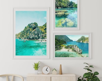 May include: Three framed photographs of tropical landscapes with turquoise water, lush green foliage, and rocky cliffs. The photos are hung on a white wall above a wooden cabinet.