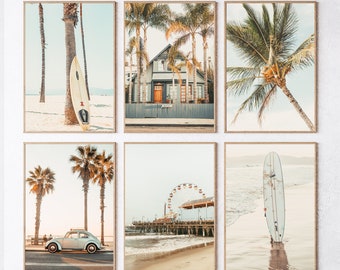 May include: Set of six framed art prints featuring coastal scenes. Images include a surfboard leaning against a palm tree, a house behind a fence, a palm tree, a vintage car, a pier with a Ferris wheel, and a surfboard on the beach.