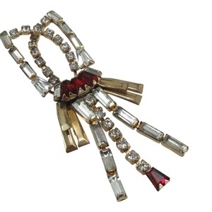 May include: A gold tone brooch with a geometric design featuring clear and red rhinestones. The brooch has a dangling tassel with clear and red rhinestones.
