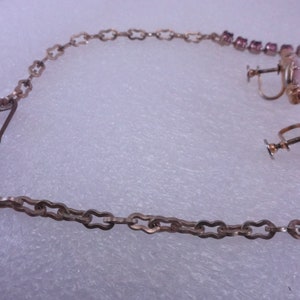 Op de afbeelding: Een zilveren ketting met een roze strass hanger en bijpassende oorbellen. De ketting heeft een sluiting en de oorbellen hebben schroefsluitingen.