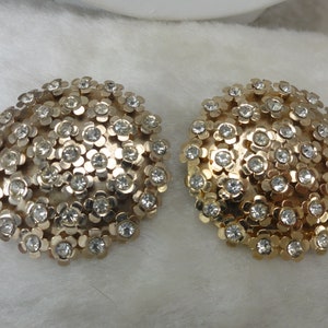 May include: A pair of gold tone clip-on earrings with a cluster of clear rhinestones in the shape of flowers.