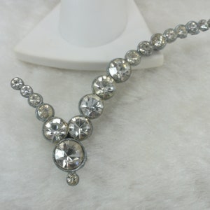May include: A silver necklace with a V-shaped design featuring clear rhinestones.
