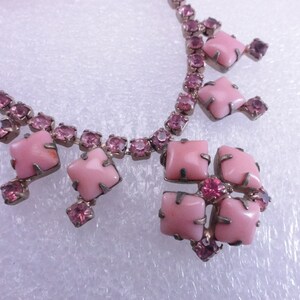 Op de afbeelding: Een roze strass ketting met een grote roze stenen hanger. De hanger is gemaakt van verschillende vierkante stenen die in zilver zijn gezet.