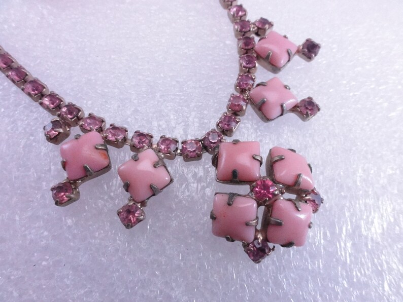 Op de afbeelding: Een roze strass ketting met een grote roze stenen hanger. De hanger is gemaakt van verschillende vierkante stenen die in zilver zijn gezet.