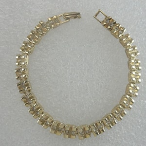 May include: Gold-toned bracelet with a repeating pattern of square links, each set with small, clear crystals. The bracelet is open, showing the clasp mechanism. A classic piece of jewelry.
