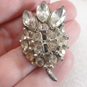 May include: A silver tone brooch with a cluster of clear rhinestones in the shape of a flower.