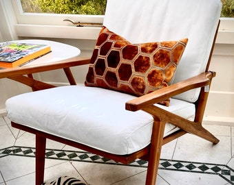May include: A white armchair with a wooden frame and a brown and gold geometric patterned cushion. The chair is sitting on a tiled floor with a zebra print rug in front of it.