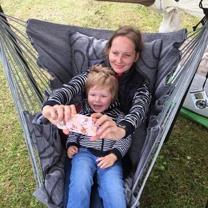 May include: A grey and black patterned fabric hanging chair with a sturdy wooden support bar at the top. The chair features a deep seat and backrest with a textured, woven design, suspended by multiple grey ropes attached to the overhead wooden beam.