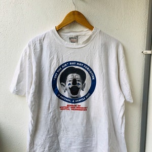 Peut inclure: T-shirt blanc avec un graphique circulaire bleu représentant un clown avec le texte "Off the Air" But Not Forgotten" JP Patches, a Seattle Hit! Museum of History and Industry Seattle, Washington"