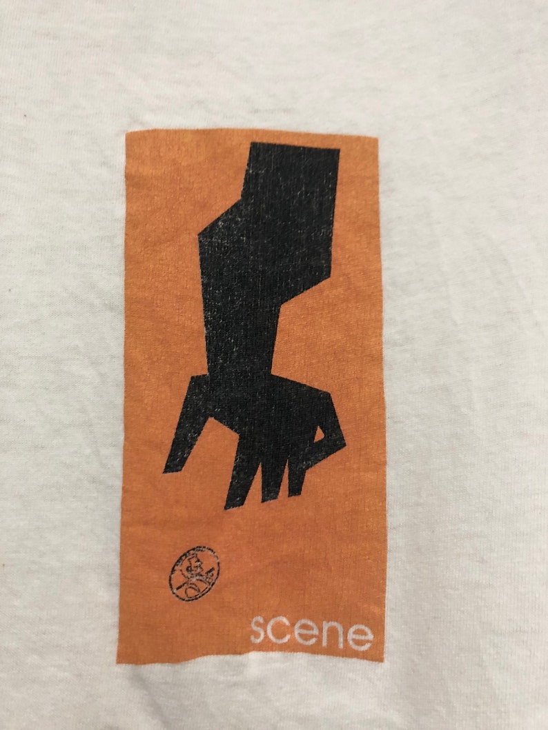 May include: A white t-shirt with a brown rectangle printed on the front. The rectangle contains a black abstract design and the word "scene" printed in white.