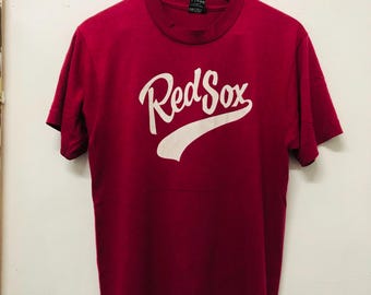 May include: A maroon t-shirt with a white "Red Sox" logo printed on the front. The logo is in a cursive font with a white baseball-shaped arc underneath.