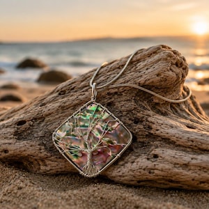 May include: A square pendant necklace featuring a wire-wrapped tree design over an iridescent abalone shell inlay. The pendant is suspended from a thin silver-toned chain, showcasing a metallic wire structure that forms the branches and trunk.