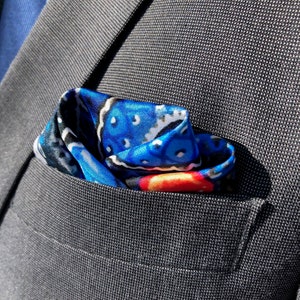 May include: A blue, red, and white patterned pocket square is folded and placed in the pocket of a gray suit jacket.