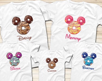 May include: Set of five white t-shirts with a donut Mickey Mouse design. The shirts say "Daddy", "Mommy", "Sister", "Brother", and "Custom".