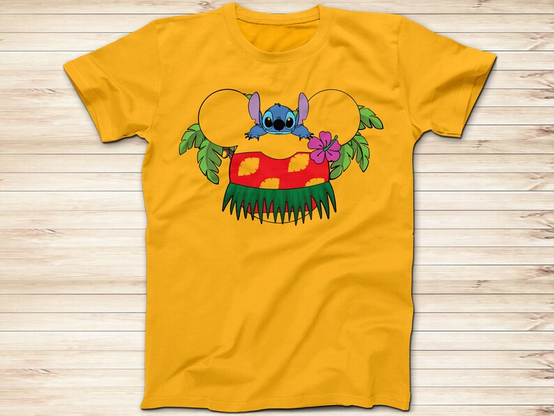 May include: Mustard yellow t-shirt featuring a cartoon graphic of Stitch from Lilo & Stitch. The design includes Stitch peeking out from behind a Mickey Mouse ear-shaped design with a red and yellow Hawaiian skirt, green palm leaves, and a pink hibiscus flower.