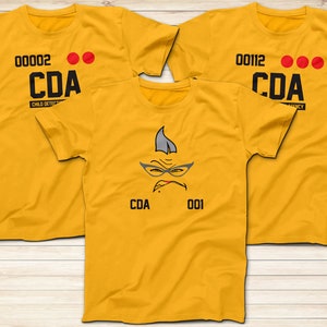 May include: Three yellow t-shirts with black text and red dots. The front of the shirts say "CDA" and have numbers. One shirt has a cartoon face with glasses and the text "CDA 001".