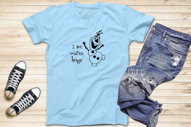 Puede incluir: Camiseta azul claro con un mu&ntilde;eco de nieve de dibujos animados negro y el texto "Me gustan los abrazos c&aacute;lidos".