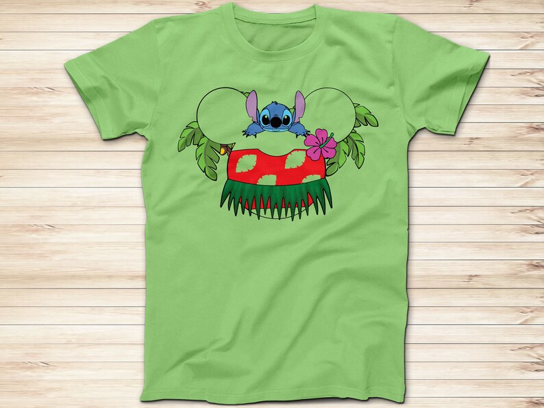 May include: A light green t-shirt featuring a cartoon graphic of Stitch from Lilo & Stitch. Stitch is depicted with a Hawaiian lei and a red and green hula skirt. The design includes Mickey Mouse ears and tropical leaves.