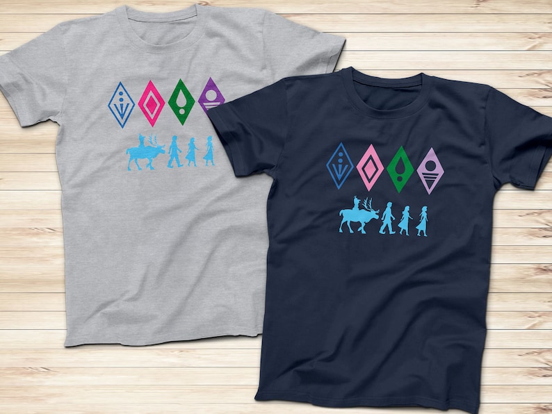 Op de afbeelding: Twee T-shirts met een grafische print van een rendier en vier figuren. De T-shirts zijn grijs en donkerblauw. De grafiek bevat vijf ruitvormige symbolen in blauw, roze, groen en paars. De tekst op de T-shirts luidt "Let It Go".