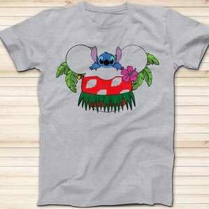May include: A light gray t-shirt featuring a colorful graphic of the character Stitch from Lilo & Stitch. Stitch is depicted in a Hawaiian-themed design, with a red and white mushroom, green grass skirt, and a pink flower. The design is in the shape of Mickey Mouse ears.