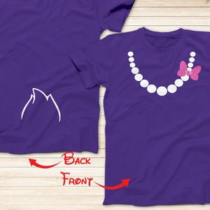May include: Two purple t-shirts with a white design. The front of one shirt has a pearl necklace with a pink bow. The back of the other shirt has a white silhouette of a mountain.