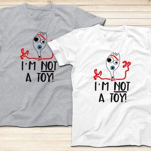 May include: Two t-shirts with a cartoon image of a fork with a face and the text "I'm not a toy!" printed on them. One shirt is grey and the other is white.