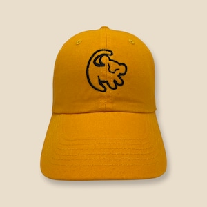 May include: A yellow baseball cap with a black embroidered lion paw print logo. The logo is a stylized image of a lion's paw print with the claws extended.