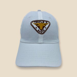 May include: White baseball cap with a brown embroidered patch featuring a bull's head and the text "Triple R Ranch".