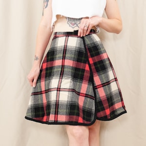 Pode incluir: Saia xadrez vintage com uma silhueta clássica em linha A. A saia apresenta um padrão arrojado de xadrez vermelho, preto, verde e creme. A bainha é finalizada com uma guarnição preta, adicionando um visual elegante a esta peça retrô.