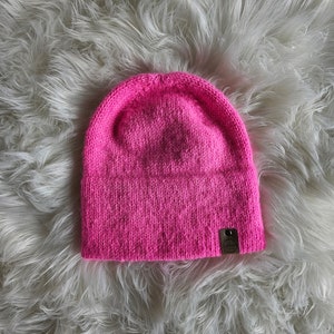 Puede incluir: Un gorro de punto de color rosa brillante con una pequeña etiqueta de cuero marrón.