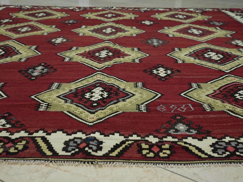 a close-up view of a vibrant, intricately patterned rug with a red background and a border of white and gold designs.