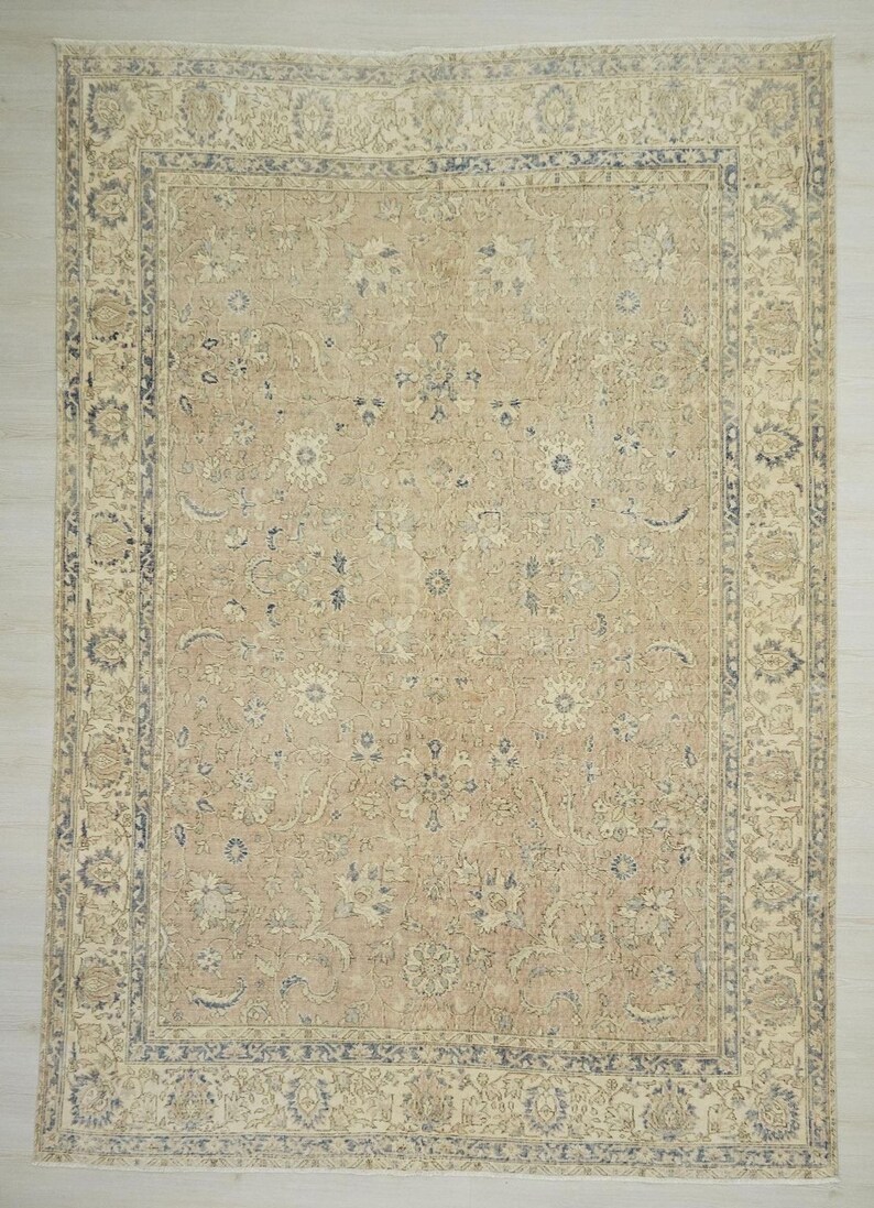 a large, intricately patterned rug with a beige and blue color scheme. The rug has a detailed design with various floral and geometric patterns, creating a visually striking and ornate appearance.