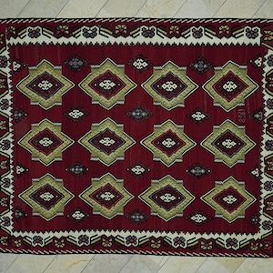 a large, intricately designed rug with a red and gold color scheme. The rug features a repeating pattern of diamond shapes in various sizes and colors, creating a visually striking and detailed design.
