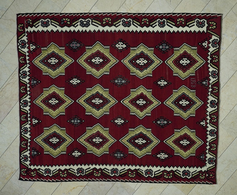 a large, intricately designed rug with a red and gold color scheme. The rug features a repeating pattern of diamond shapes in various sizes and colors, creating a visually striking and detailed design.