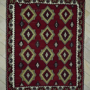 a large, intricately designed rug with a red and gold color scheme. The rug has a repeating pattern of diamond shapes in various sizes and colors, creating a visually striking and detailed design.