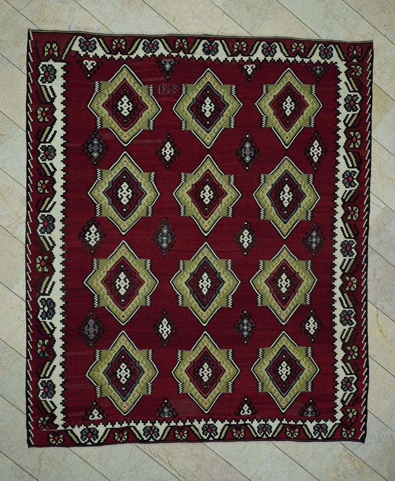 a large, intricately designed rug with a red and gold color scheme. The rug has a repeating pattern of diamond shapes in various sizes and colors, creating a visually striking and detailed design.