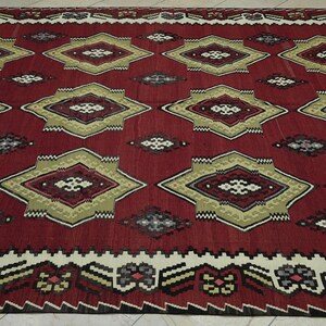 a large, intricately designed rug with a red and gold color scheme. The rug features a repeating pattern of diamond shapes in various sizes and colors, creating a visually striking and detailed design.
