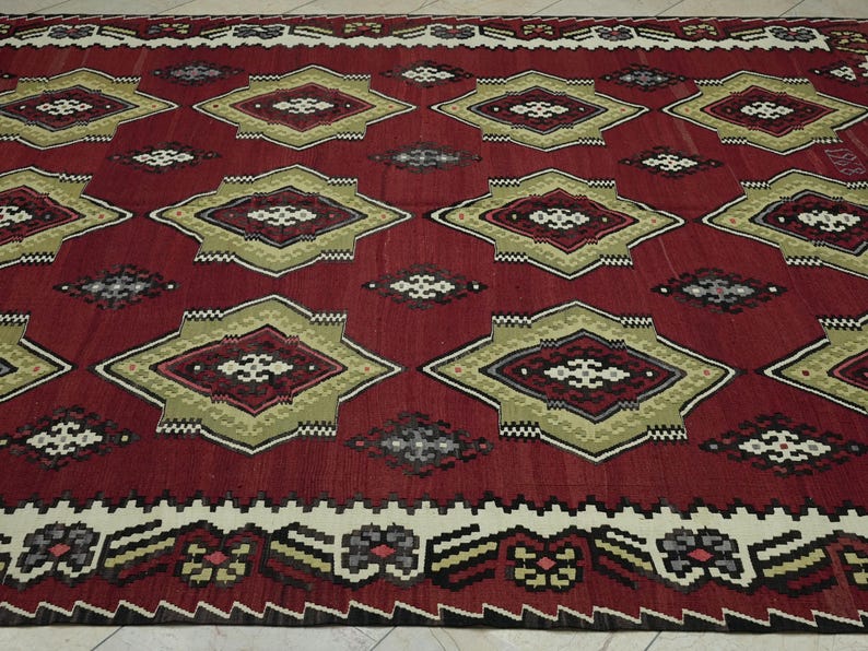 a large, intricately designed rug with a red and gold color scheme. The rug features a repeating pattern of diamond shapes in various sizes and colors, creating a visually striking and detailed design.