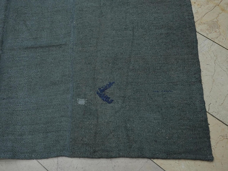 a close-up view of a dark-colored fabric, possibly a blanket or rug, placed on a tiled floor.