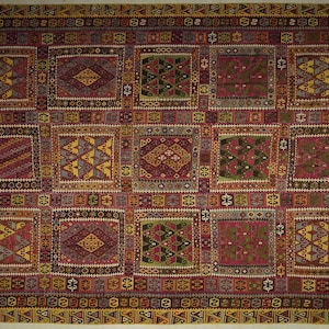 The image is a large, colorful, and intricate textile or rug with a repeating pattern of geometric shapes and designs in various colors, including red, yellow, green, and blue.