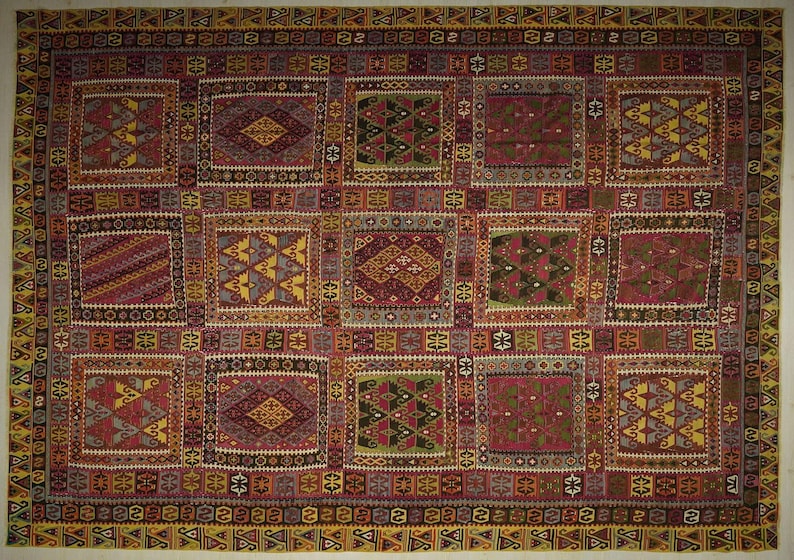 The image is a large, colorful, and intricate textile or rug with a repeating pattern of geometric shapes and designs in various colors, including red, yellow, green, and blue.