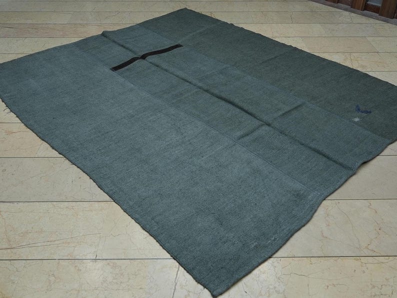 a large, square-shaped, dark green textile with a black line running through the center, lying on a tiled floor.