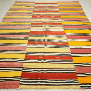 a large, colorful rug with a variety of stripes in different colors, including red, yellow, and black. The rug is placed on a white floor, creating a striking contrast between the vibrant colors and the neutral background.