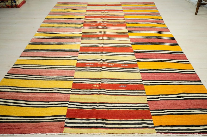 a large, colorful rug with a variety of stripes in different colors, including red, yellow, and black. The rug is placed on a white floor, creating a striking contrast between the vibrant colors and the neutral background.