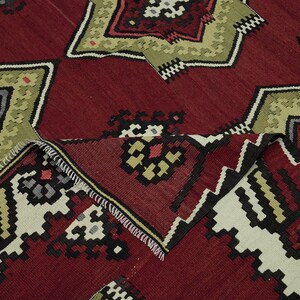 a close-up view of a vibrant, intricately patterned rug with a mix of red, green, and black colors. The rug features a variety of geometric shapes and designs, creating a visually striking and detailed appearance.