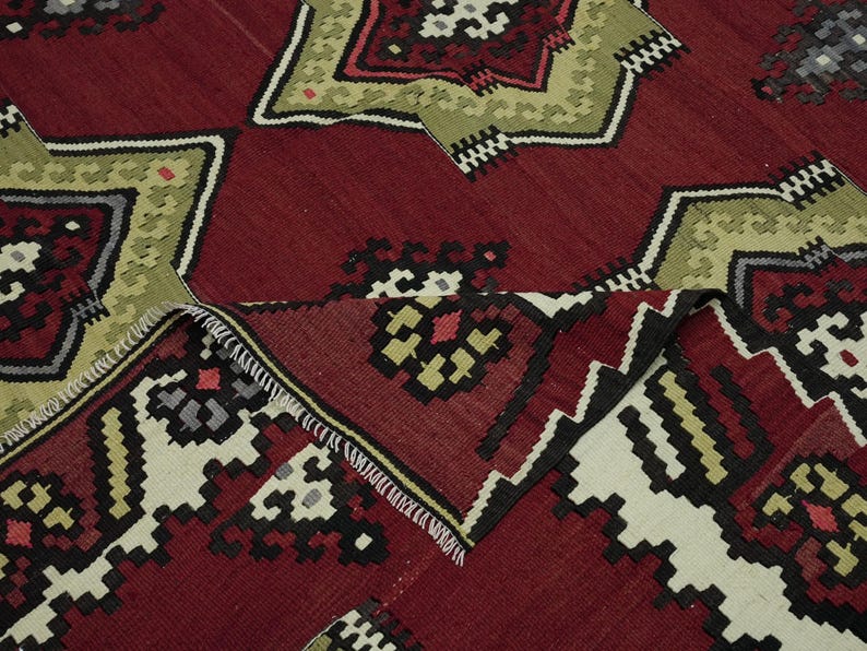 a close-up view of a vibrant, intricately patterned rug with a mix of red, green, and black colors. The rug features a variety of geometric shapes and designs, creating a visually striking and detailed appearance.